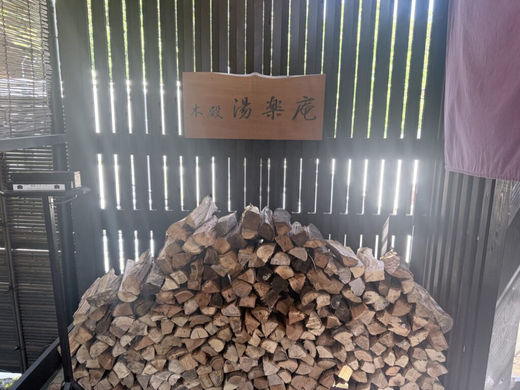 箱根湯寮の館内に配置された、紫のアリウムや黄色いユリの豪華な生け花と、その下に整然とストックされたサウナ用の薪。自然素材による物理ストレージと彩りのマッピング。