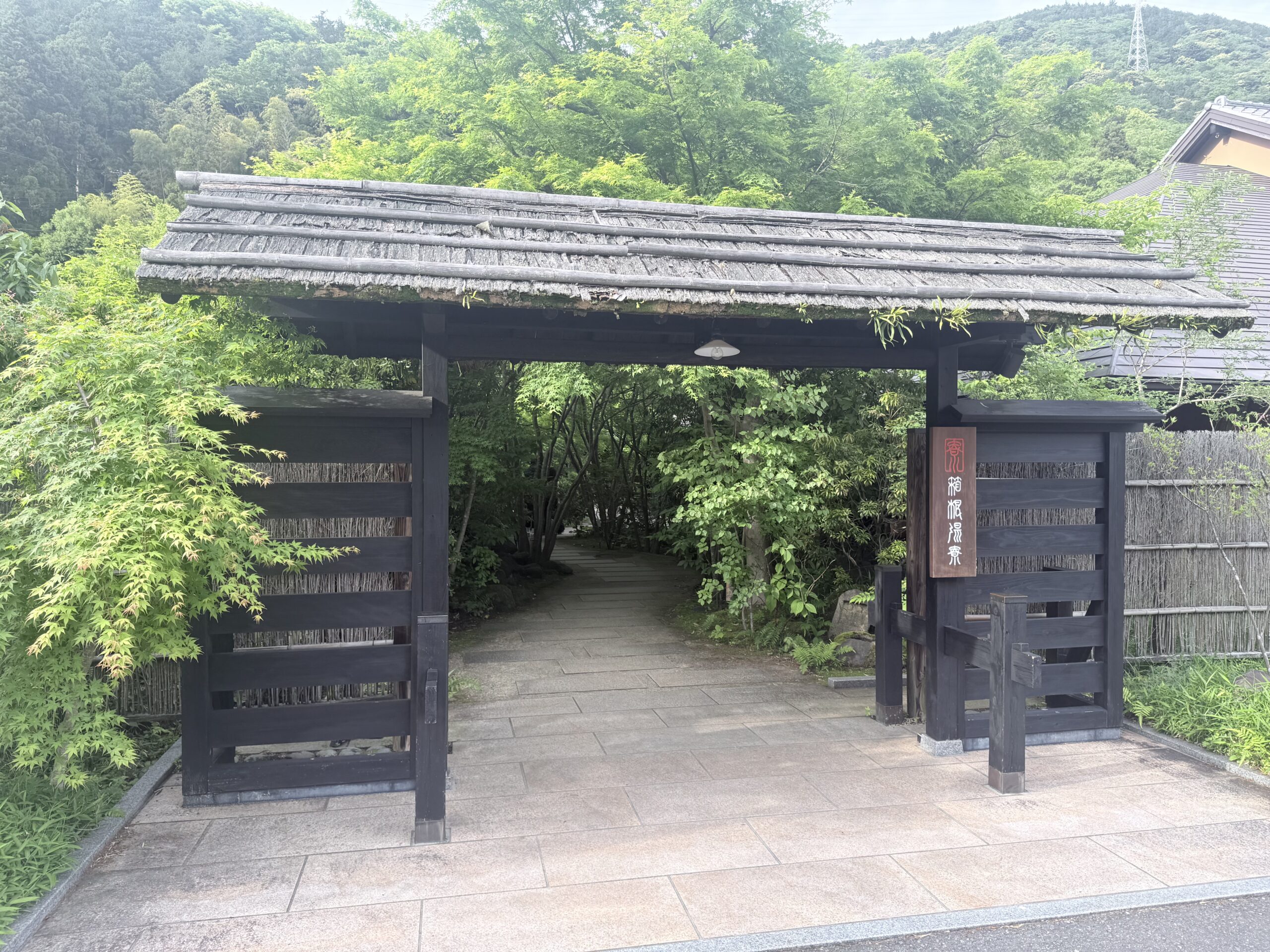 古民家風の立派な門構えの「箱根湯寮」入り口。新緑に囲まれた情緒あるエントランスで、サウナと温泉のデバッグ開始を予感させる景観。